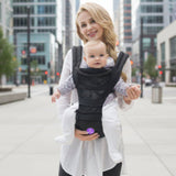 Woman carrying a baby in a black carrier on a city street.