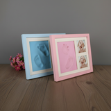 Two baby hand and footprint frames, one blue and one pink, on a wooden surface.