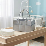 Gray fabric storage basket on a wooden surface with baby items in a nursery setting.