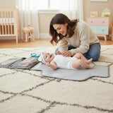Gray baby changing bag with multiple compartments and a baby on a mat.